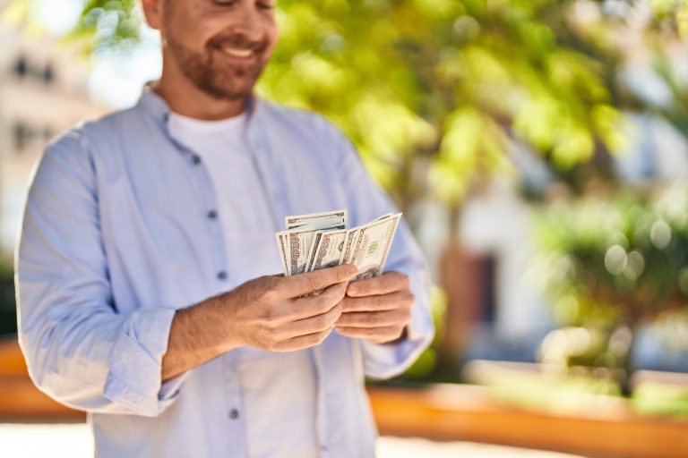 Young caucasian man smiling confident counting dollars at park - Sincere Moneylender