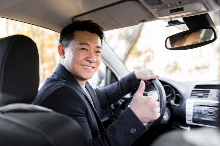 A man driving an Asian car behind the wheel looks at the camera and smiles - Sincere Moneylender