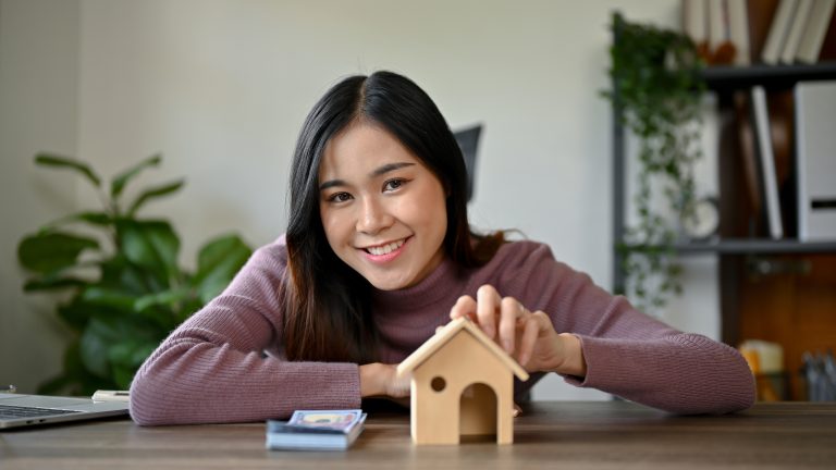 young Asian girl with house model planning on buying her house - Sincere Moneylender