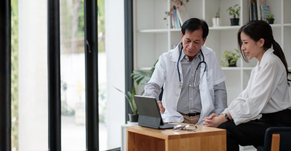A Senior asian doctor is consulting with a young female patient, talking to the client at a medical checkup visit. Geriatric diseases treatment. Elderly medical health care concept.